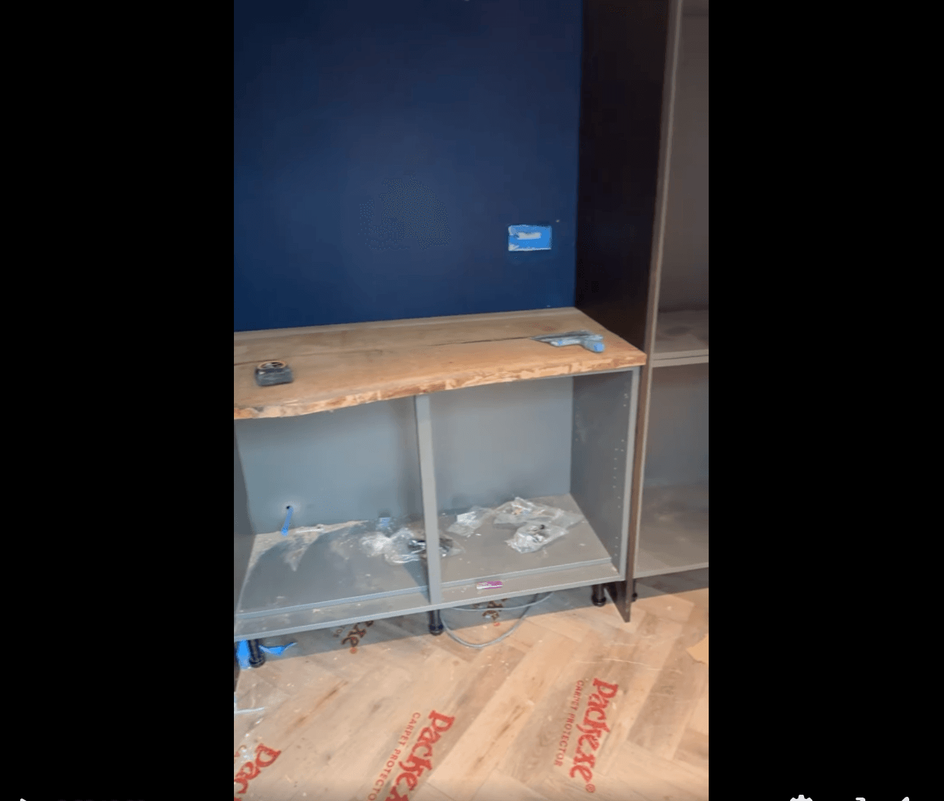 Built-in shelving unit being installed against a navy feature wall on a fresh herringbone floor.