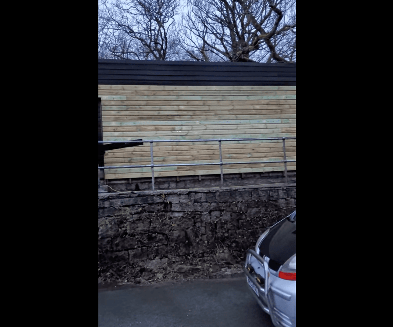 New timber cladding panels being fitted to an outbuilding behind a stone wall.