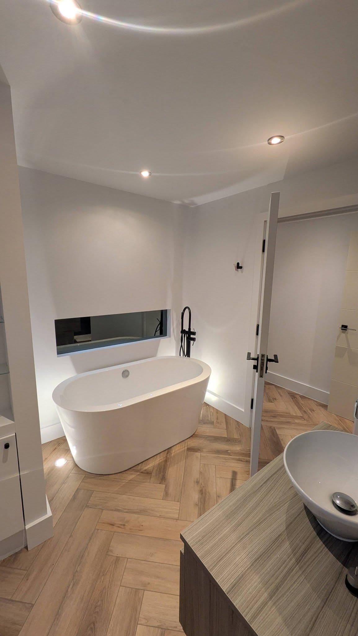Modern bathroom with freestanding tub, mirrored niche and herringbone floor.
