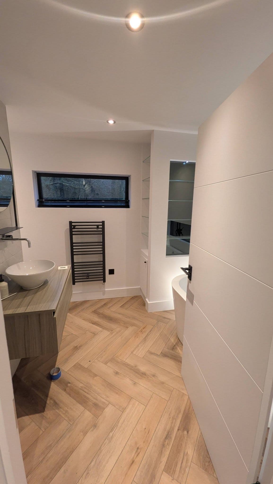 Bathroom with vessel sink on timber-effect vanity, black heated towel rail and herringbone floor.