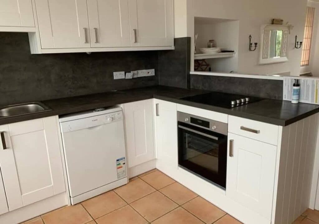 White shaker kitchen with dark stone-effect worktops and slate splashback.