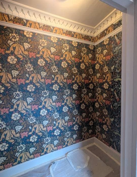 Period room hung with William Morris-style navy and ochre floral wallpaper, original cornicing preserved.