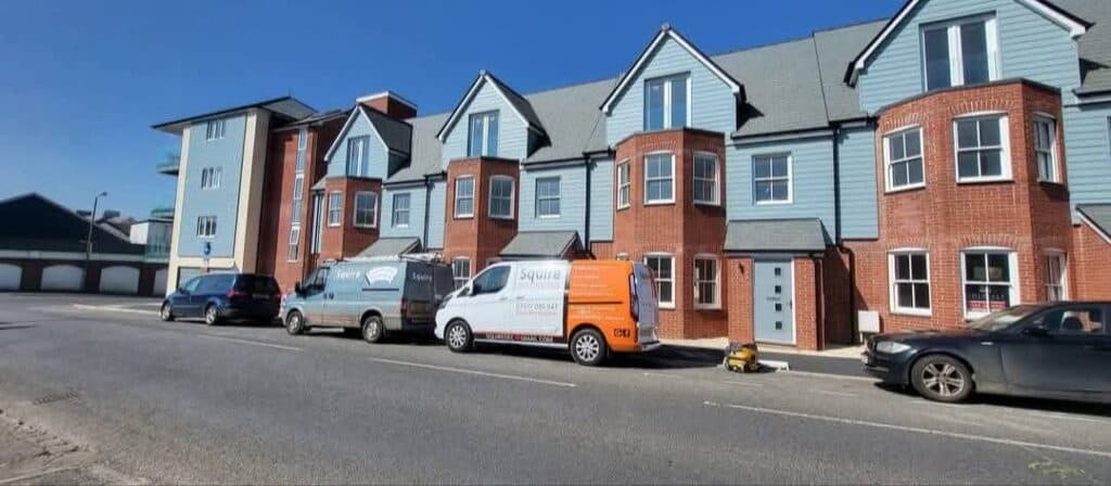 Branded Squire Decorating vans parked outside a row of newly-finished blue and red brick terrace houses.