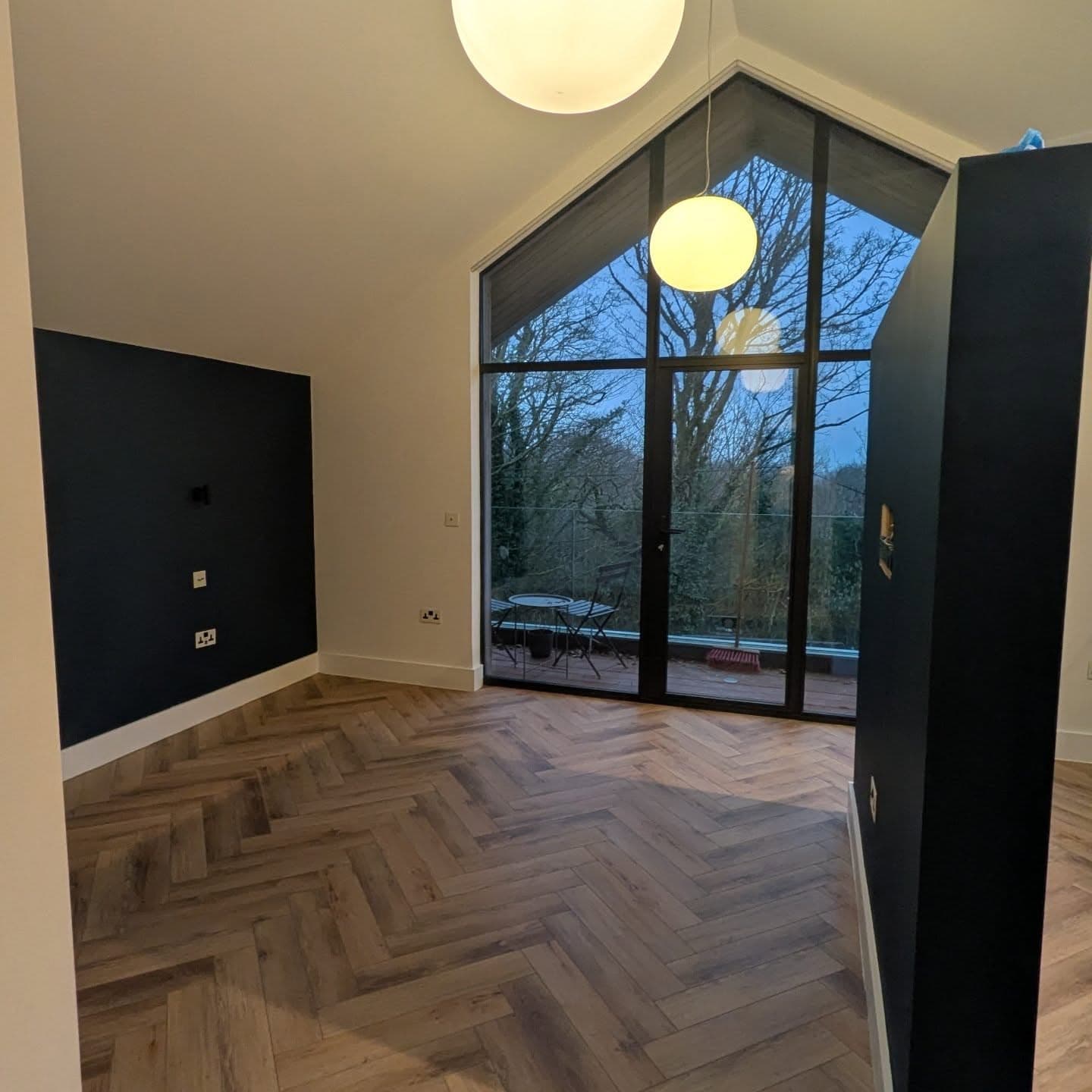 Vaulted living room with herringbone parquet and a full-height apex window onto the garden.
