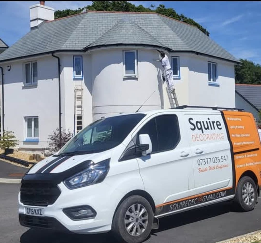 Roy Squire on a ladder painting a property in Bude with the branded Squire Decorating van parked outside.